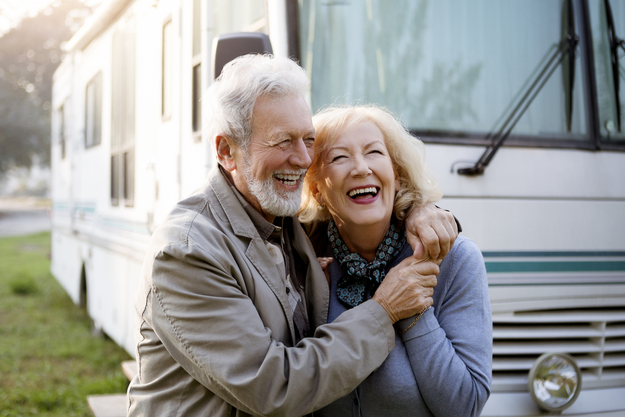 senior couple laughing and smiling in front of large rv getting ready for an rv road trip