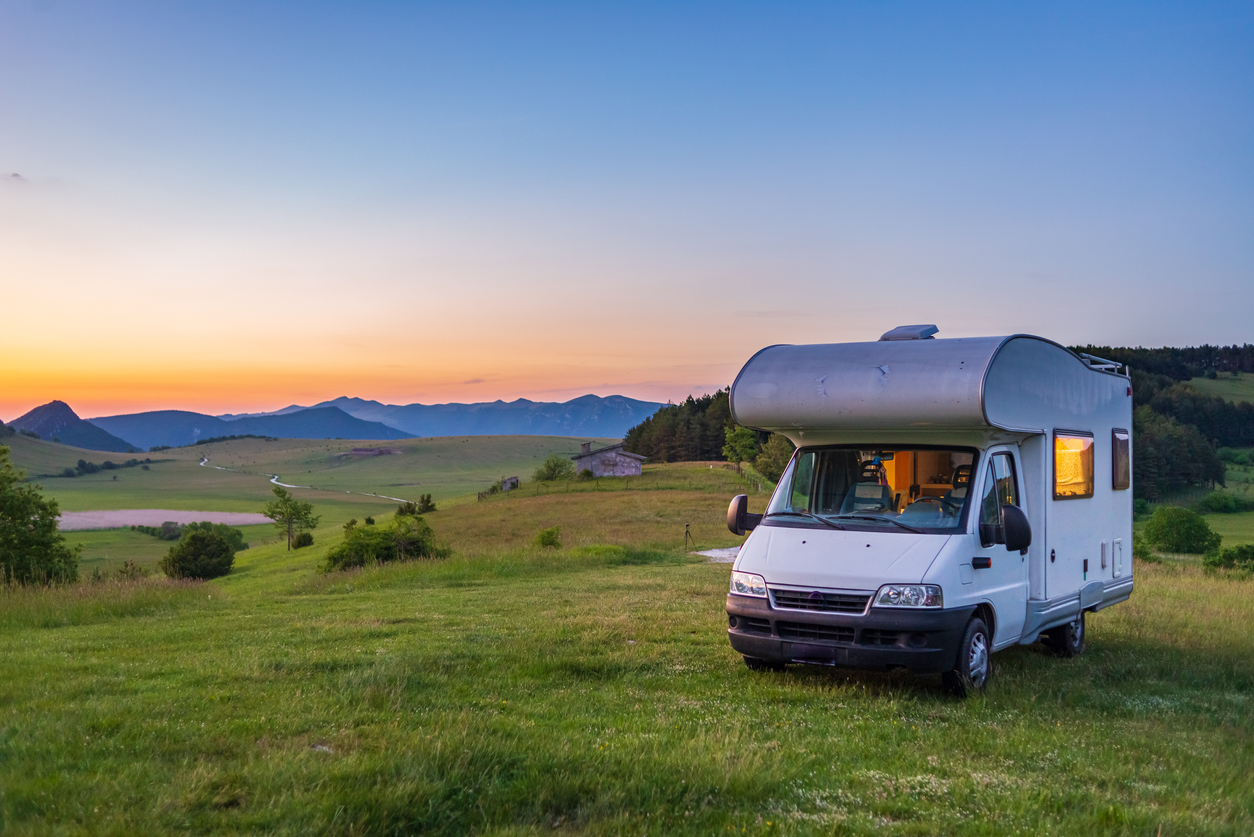 small camper rv parked on grassy hill with sunset in the background boondocking